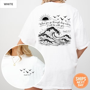 May include: A white t-shirt featuring a black graphic on the back of a sun, birds, and ocean waves with the text "When you go through deep waters, I will be with you. Isaiah 43:2". The front chest area displays a small graphic of birds and "Isaiah 43:2".