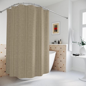 May include: A beige shower curtain with vertical stripes hangs from a curved, silver-colored rod. The curtain has a subtle floral pattern. The bathroom features a white bathtub, a small table, and a framed artwork with red and black accents.