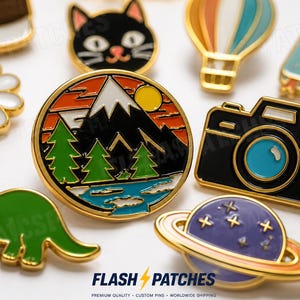Puede incluir: Una colección de pines de esmalte coloridos con varios diseños, incluyendo un paisaje de montaña, una cámara negra, un dinosaurio verde, un planeta morado con anillos, una margarita, una cara de gato negro, un globo aerostático y un letrero con GOOD VIBES.