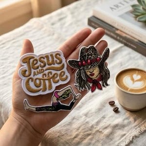Puede incluir: Una mano sostiene tres parches bordados: "Jesus and Coffee" en hilo dorado, una vaquera con sombrero de estampado de leopardo y una persona haciendo yoga. También se ve una taza de café con arte latte y granos de café.