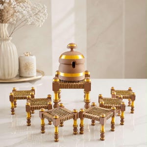 May include: A brown and gold honey pot with a lid sits atop a small, woven-top stool with four legs. Surrounding this central piece are seven additional small, matching stools with woven tops and brown and gold legs, arranged in a semi-circle.