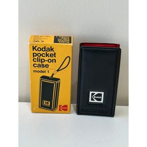 Puede incluir: Un estuche Kodak Pocket Clip-On, modelo 1, vintage, con su caja original amarilla y negra. La caja presenta el logotipo de Kodak e información del producto. Junto a él, un estuche de cuero negro con interior rojo y el logotipo de Kodak.