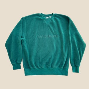 May include: A long-sleeved forest green fleece sweatshirt featuring a crew neckline and a triangular ribbed insert below the collar. The text GAP ATHLETIC is embroidered in a matching green thread across the centre of the chest area.