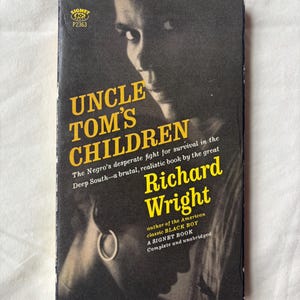 May include: A vintage paperback book titled "Uncle Tom's Children" by Richard Wright. The cover features a black and white image of a person's face and the title in yellow lettering. The book is a Signet Book.