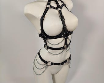 May include: A black leather harness featuring a choker collar, adjustable straps with silver-toned metal buckles, circular rings, and multiple draped silver-toned chains connecting the chest and waist sections on a mannequin.