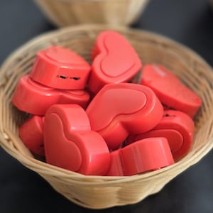 Könnte beinhalten: Ein Weidenkorb gefüllt mit mehreren roten herzförmigen Objekten. Die Herzen haben eine glatte, glänzende Oberfläche und sind zusammen gestapelt. Der Korb besteht aus gewebtem, hellfarbigem Material.