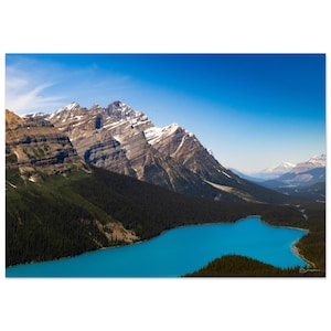 Peut inclure: Photographie de paysage d'un lac turquoise entouré de forêts vertes luxuriantes et de montagnes enneigées imposantes sous un ciel bleu clair. L'image capture un environnement naturel serein.