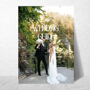 Puede incluir: Una guía de bodas con el título "The Wedding Guide" en letras blancas. La imagen muestra a una pareja en un balcón con un fondo escénico. El novio sostiene un ramo de flores blancas y la novia lleva un vestido de novia blanco.