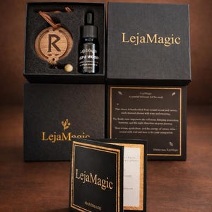 May include: An assortment of black boxes with gold lettering and a wooden charm. The boxes contain a bottle of oil, a wooden charm with the letter "R", and informational cards. The brand name "LejaMagic" is visible.