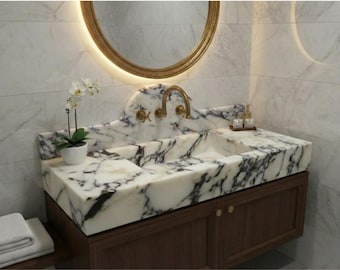 May include: A luxurious bathroom vanity with a marble countertop featuring black veining. The vanity has a built-in sink, gold fixtures, and a wooden cabinet base. A gold-framed mirror and a potted orchid complete the elegant design.