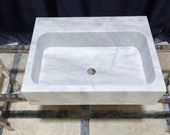 Könnte beinhalten: Ein rechteckiges Waschbecken aus weißem Marmor mit einem zentralen Abflussloch. Das Waschbecken hat eine glatte, polierte Oberfläche und wird von einem Metallrahmen getragen. Der Marmor hat subtile graue Maserungen. Ideal für Badezimmerrenovierungen.