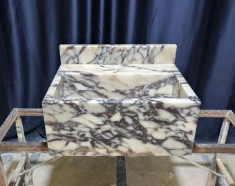 Peut inclure: Un évier rectangulaire en marbre avec un dosseret. L'évier présente une base blanche avec des veines violet foncé. L'évier est monté sur un cadre métallique. L'arrière-plan est un rideau bleu foncé.