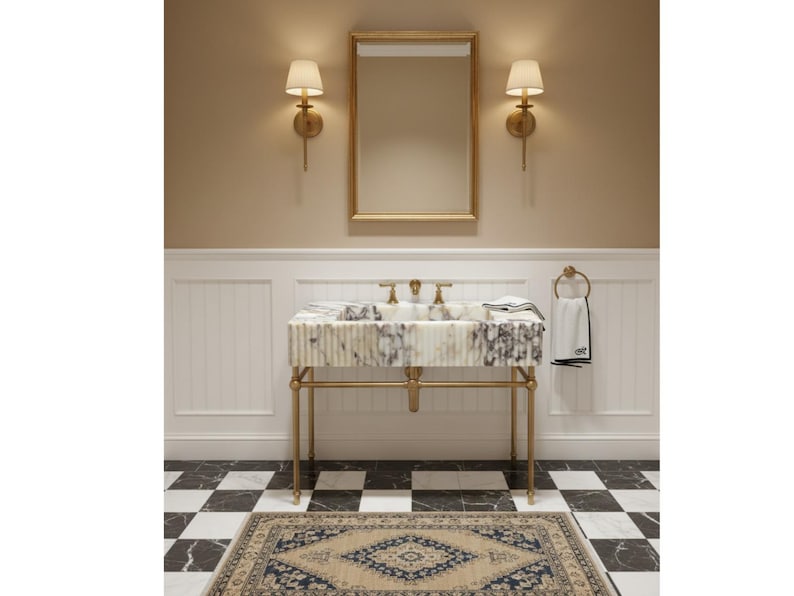 Puede incluir: Interior de ba&ntilde;o con lavabo de m&aacute;rmol sobre soporte dorado, grifer&iacute;a dorada y espejo. Las paredes beige tienen apliques. Una alfombra estampada y un suelo ajedrezado en blanco y negro completan el dise&ntilde;o.