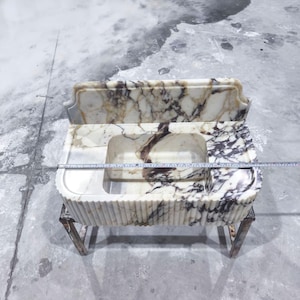 May include: A marble sink with a rectangular basin and a matching backsplash. The sink has a cream and brown veined pattern and is supported by a metal frame. The sink's dimensions are approximately 36 inches wide.