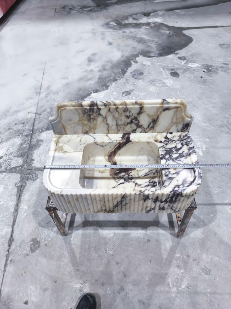 May include: A marble sink with a rectangular basin and a matching backsplash. The sink has a cream and brown veined pattern and is supported by a metal frame. The sink's dimensions are approximately 36 inches wide.