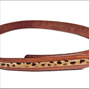 May include: A brown leather belt featuring a central inlay of animal print hair-on hide. The belt has smooth, stitched leather edges framing the textured, spotted pattern that runs along the length of the strap, showcasing a classic design.