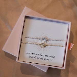 May include: A pair of delicate bracelets, one silver and one gold, each featuring celestial designs of the sun and moon. The bracelets are displayed in a pink gift box with the inscription "You are my sun, my moon, and all of my stars".