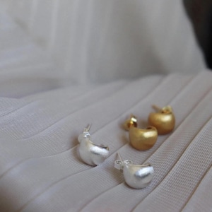 Peut inclure: Gros plan sur quatre boucles d'oreilles, deux argentées et deux dorées. Les boucles d'oreilles ont un design arrondi et abstrait. Les boucles d'oreilles argentées sont à gauche et les boucles d'oreilles dorées à droite. Bijoux.