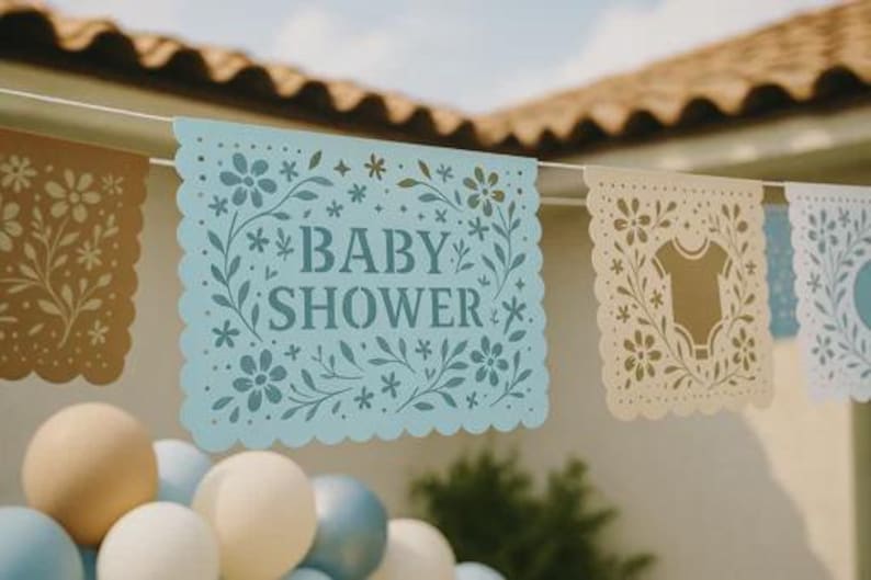 以下が含まれることがあります： スカラップエッジのライトブルーの紙製バナー。ダークブルーのフォントで「BABY SHOWER」という文字が記され、複雑な花の切り抜きが施されています。バナーは白い紐で吊るされており、花やベビー服の柄が描かれた他の装飾パネルと並んでいます。