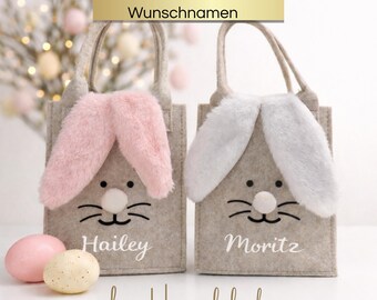 May include: Two gray felt Easter bags with bunny ears, one pink and one white. Each bag has a bunny face and a name printed on it. A pink and a speckled egg are in front of the bags. The text "Personalizable with desired names" is at the top.
