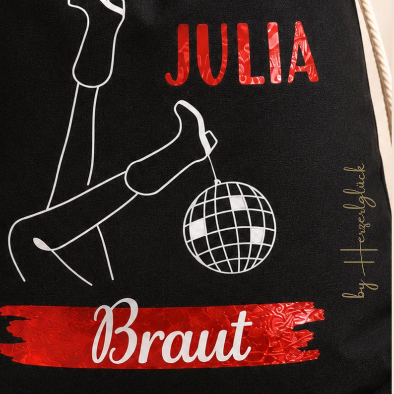 Puede incluir: Bolsa con cord&oacute;n negra con ilustraci&oacute;n blanca de piernas y una bola de discoteca. El nombre "JULIA" est&aacute; en rojo, y la palabra "Braut" est&aacute; en blanco sobre una pancarta roja. El texto "by Herzergl&uuml;ck" es dorado.