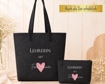 May include: A dark gray tote bag and matching zippered pouch. Both items feature the word "LEHRERIN" and the name "Frau Brunner" with a pink heart. The tote bag has black handles. The text "Geschenk Lehrerin mit Herz" and "Auch als Set erhältlich" are also visible.