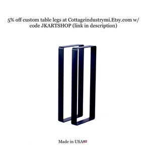 May include: Two black metal table legs, each with a rectangular shape, are shown against a white background. The legs are made in the USA.
