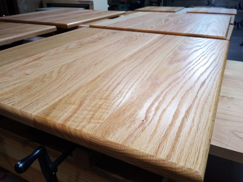 May include: Close-up of a light wood table top with a smooth, polished finish. The grain of the wood is visible and the surface is slightly curved at the edges.