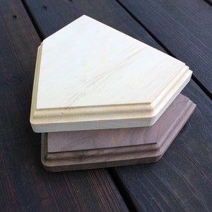 May include: Two wooden home plate bases, one light brown and one dark brown, stacked on top of each other. The bases are on a dark wood surface.