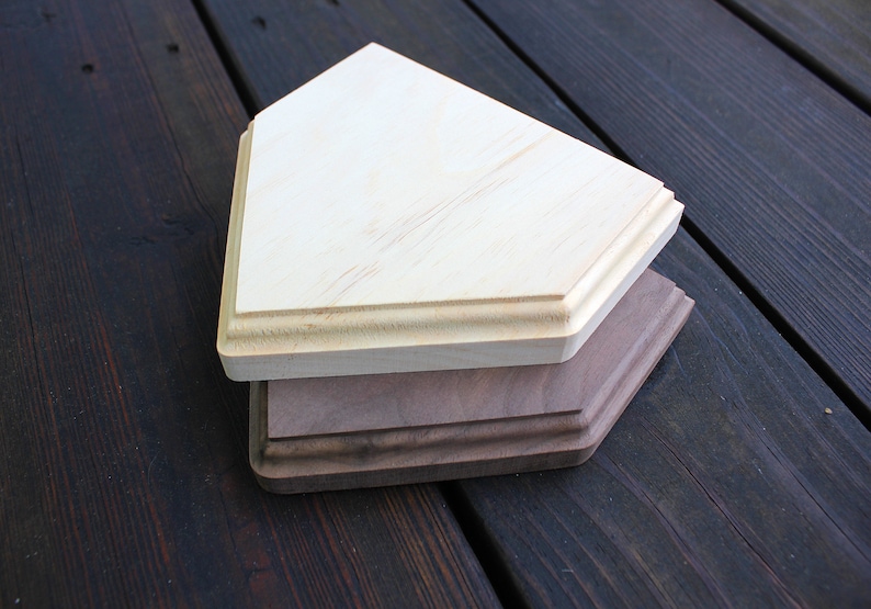 May include: Two wooden home plate bases, one light brown and one dark brown, stacked on top of each other. The bases are on a dark wood surface.
