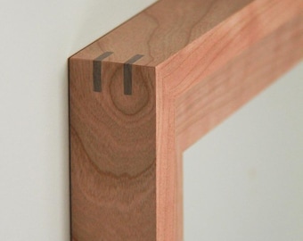 May include: A rectangular wooden frame featuring a light brown natural wood grain pattern. The corner joint is reinforced with two dark, thin, rectangular splines embedded into the wood, creating a clean and precise mitered corner connection.
