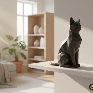 Könnte beinhalten: Eine schwarze, geometrische Katzenskulptur. Die Katze sitzt aufrecht mit aufgestellten Ohren. Die Skulptur besteht aus vielen flachen Oberflächen, was ihr ein modernes, kantiges Aussehen verleiht. Die Katze steht auf einer weißen Oberfläche.