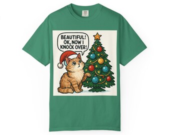 Puede incluir: Camiseta verde con un gato de dibujos animados con un gorro de Papá Noel, junto a un árbol de Navidad decorado. El gato mira hacia arriba con un bocadillo que dice: "BEAUTIFUL! OK, NOW I KNOCK OVER!"