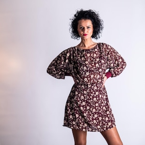 May include: A burgundy floral print dress with long sleeves and a matching skirt. The dress features a round neckline and a fitted waist. The sleeves have a burgundy cuff. The dress is made of a sheer fabric with a white floral pattern.
