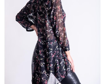 May include: Black floral print tunic top with a high collar and long sleeves. The sheer fabric features a pattern of small red and white flowers. The tunic is paired with black leather pants.