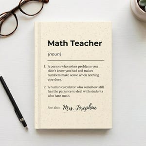 May include: A beige notebook with the text "Math Teacher" and a definition. The notebook also includes the text "See also: Mrs. Josephine". A pair of eyeglasses, a pen, and a small potted plant are also visible.