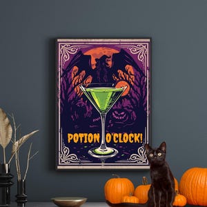 Op de afbeelding: Een ingelijste Halloween-print met een groene cocktail, de woorden "POTION O'CLOCK!" en een heksensilhouet. Een zwarte kat zit op een houten kast met oranje pompoenen. De print heeft een donkerblauwe achtergrond.