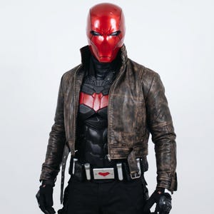 May include: A glossy red full-face helmet paired with a distressed brown leather jacket, a black tactical chest piece with a red emblem, black gloves, and a utility belt featuring silver canisters and a central buckle with a red bat-like symbol.