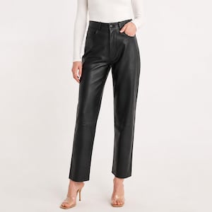 Könnte beinhalten: Schwarze Lederhose mit geradem Bein. Die Hose hat einen klassischen Fünf-Taschen-Stil und einen Knopf- und Reißverschluss. Das Model trägt ein weißes Langarmshirt und transparente Absätze.