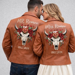 May include: Two tan leather jackets with embroidered designs. Each jacket features a steer skull with roses, hearts, and the date 09.17.2024. One jacket says "MR. Romeo" and the other says "Mrs. Romeo".