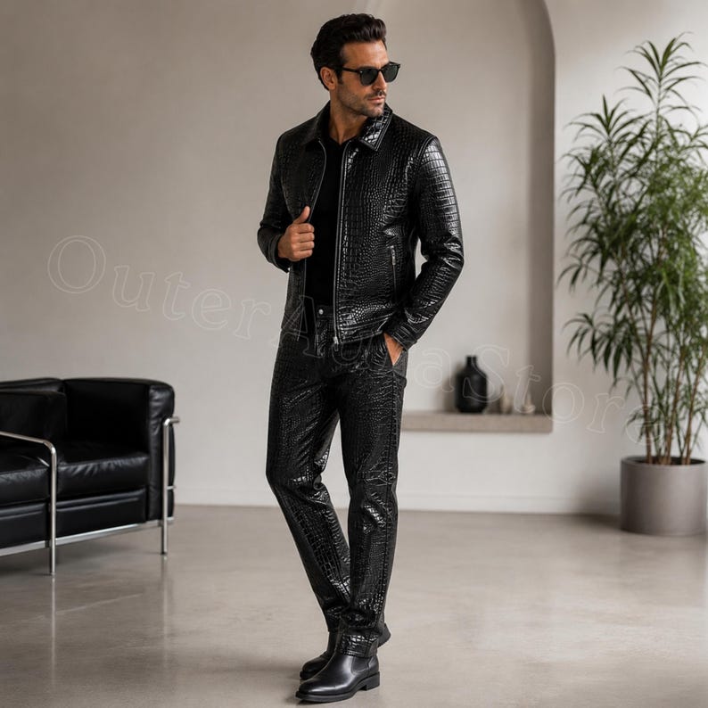May include: A black jacket and matching trousers set featuring a textured crocodile skin pattern. The jacket has a collared neckline, a front zipper closure, and long sleeves. The trousers are straight-legged and feature the same embossed finish.