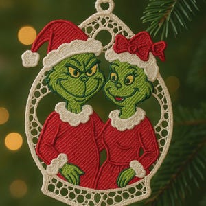 May include: Embroidered Christmas ornament featuring a green character with a red Santa hat and a matching character with a red bow. Both characters are wearing red outfits with white trim. The ornament is framed in a white, openwork design.