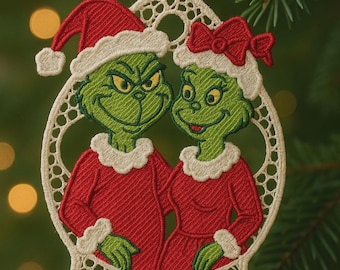 May include: Embroidered Christmas ornament featuring a green character with a red Santa hat and a matching character with a red bow. Both characters are wearing red outfits with white trim. The ornament is framed in a white, openwork design.