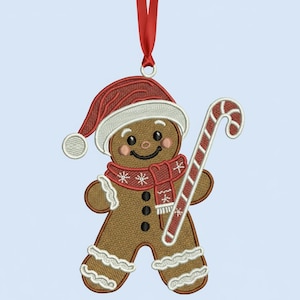 Può includere: Ornamento natalizio ricamato a forma di omino di pan di zenzero. L'ornamento presenta un omino di pan di zenzero con cappello e sciarpa di Babbo Natale, che tiene in mano un bastoncino di zucchero. L'ornamento è marrone, rosso e bianco, con un nastro rosso per appenderlo.