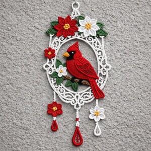 May include: A handcrafted wall hanging featuring a red cardinal bird perched on a branch within a white, ornate oval frame. The frame is adorned with red and white flowers and green leaves, with dangling red teardrop accents.