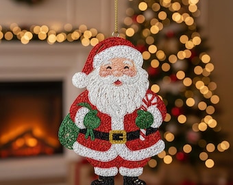 May include: A Christmas ornament featuring Santa Claus, with a red suit, white beard, and a candy cane. Santa is holding a green bag and wearing a black belt with a gold buckle. The ornament is hanging from a gold string.