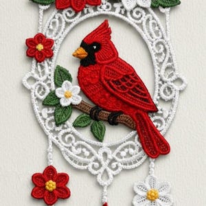 May include: A handcrafted, red cardinal bird perched on a brown branch, surrounded by white lace and red and white flowers. The bird has a black mask and orange beak. The design is framed by a white, ornate oval shape, with hanging red teardrop accents.