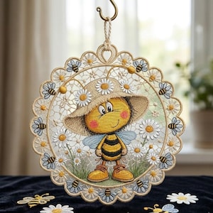 Può includere: Decorazione murale rotonda ricamata con un'ape dei cartoni animati con un cappello di paglia, circondata da margherite e altre api. Il disegno è incorniciato da un bordo smerlato con dettagli di api e margherite. Appeso a un gancio dorato.