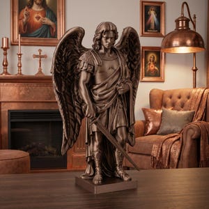 Puede incluir: Una estatua de color bronce de un ángel con grandes alas, que lleva una armadura de estilo romano y una túnica drapeada. La figura se alza sobre una base rectangular, sosteniendo una espada hacia abajo con la mano derecha, mano izquierda cerca del pecho.