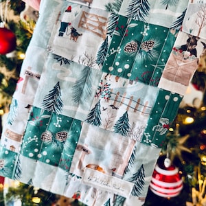 May include: A patchwork fabric item with a Christmas theme, showing winter landscapes, pine trees, and farm scenes. The design uses green, white, and brown colours. The item is handmade, with the text "by The Rooke Brothers" visible.